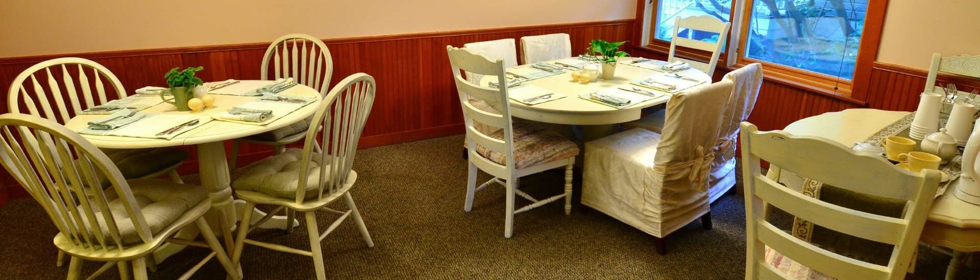A cozy dining area featuring round tables set with utensils and decorative plants.