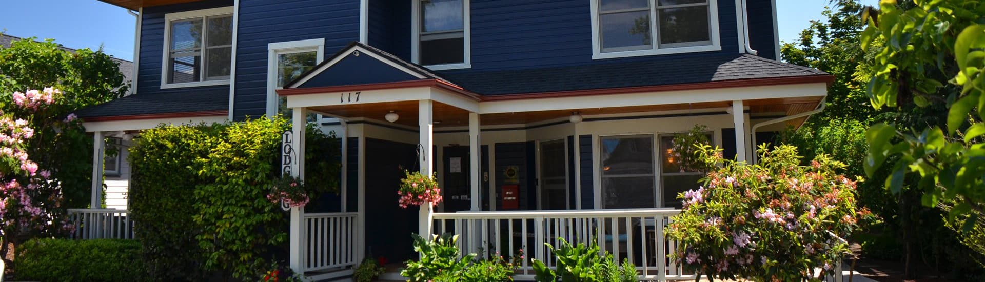 A charming blue house with a front porch surrounded by lush greenery and flowers.