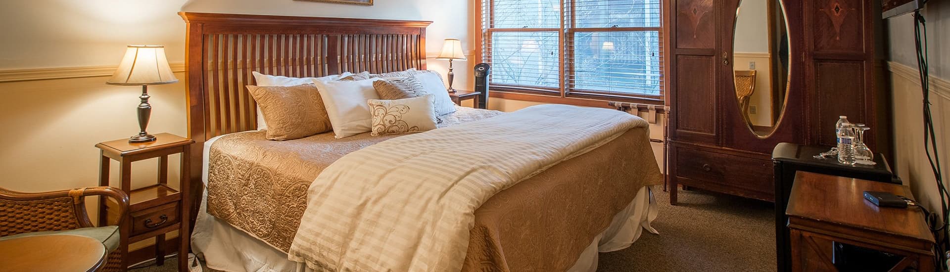 Cozy bedroom featuring a large bed, decorative pillows, a wooden wardrobe, and natural light from a window.