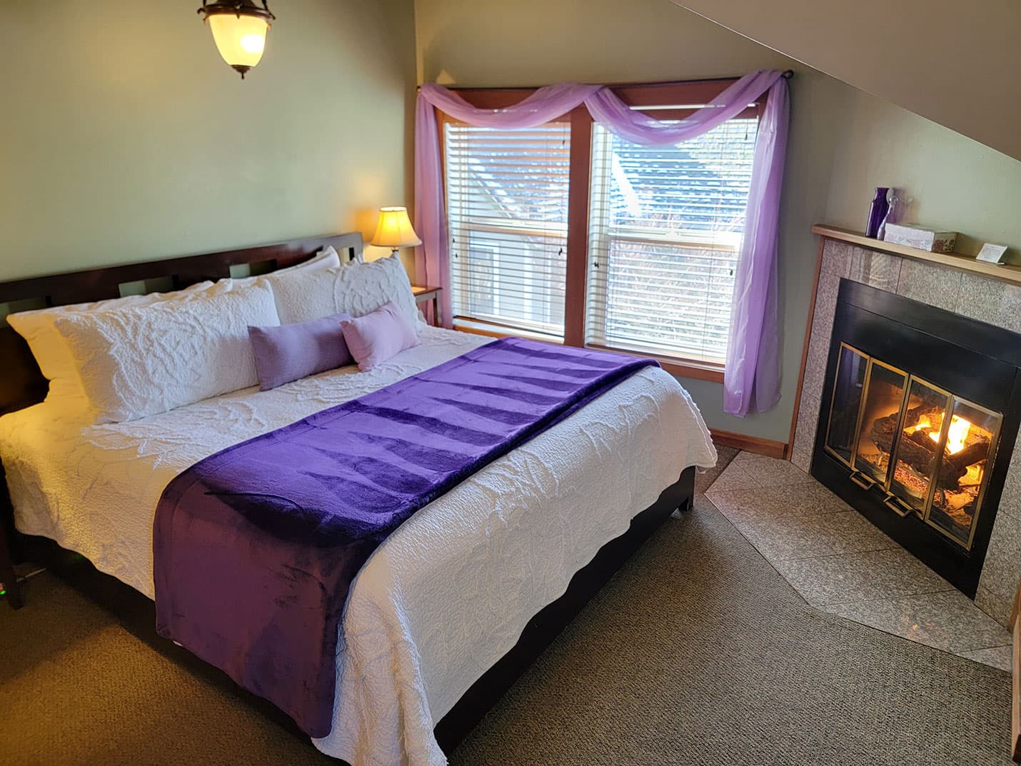 Cozy bedroom with a fireplace, purple accents, and large windows.