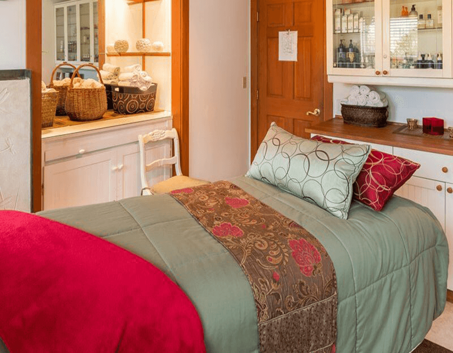 A neatly arranged bedroom featuring a green quilted bedspread, decorative pillows, and a wooden cabinet with towels and baskets.