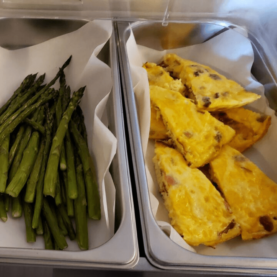 A tray of cooked asparagus next to slices of omelette in a food container.