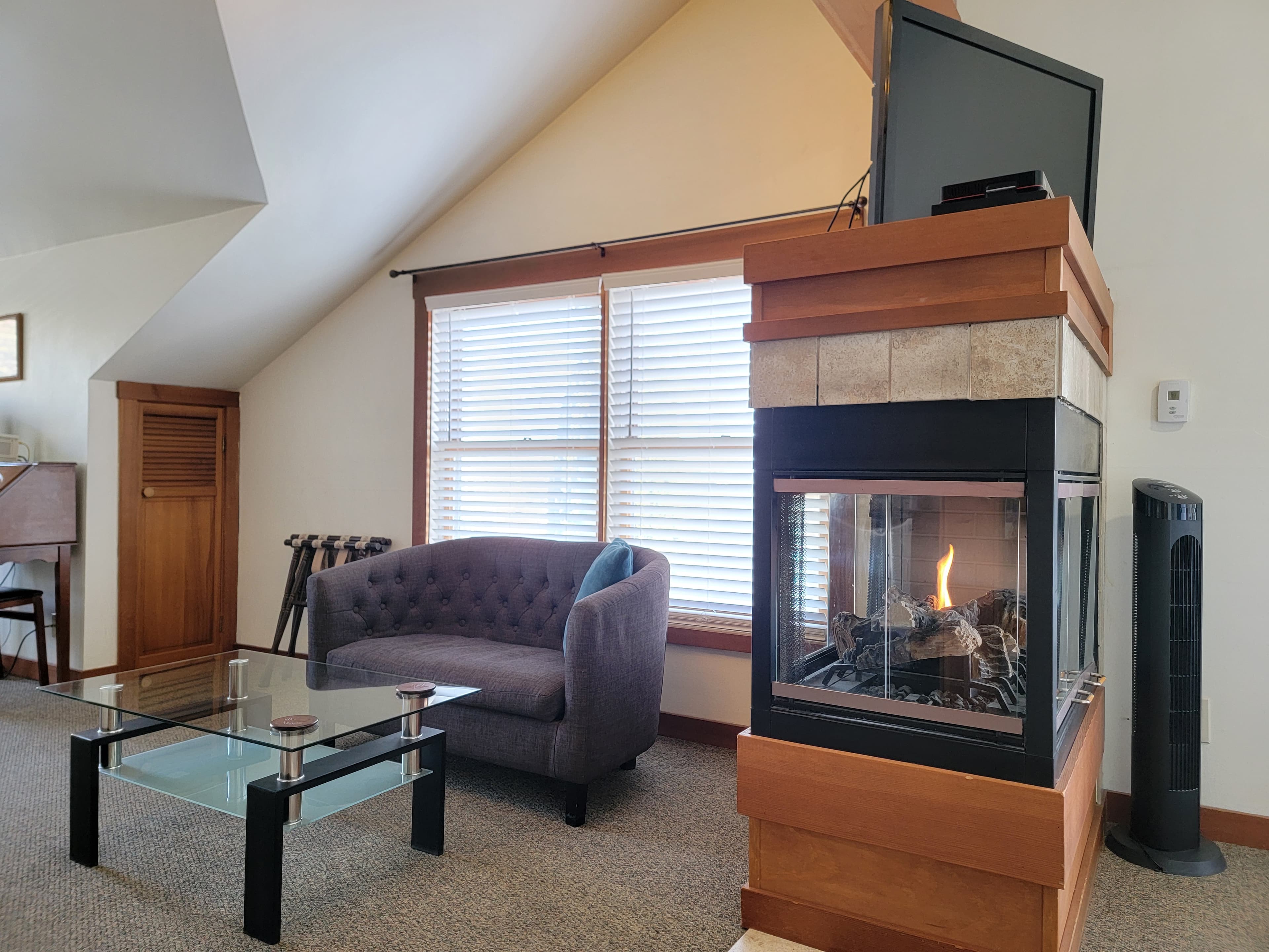 Cozy living room featuring a fireplace, a glass coffee table, and a gray couch near large windows.