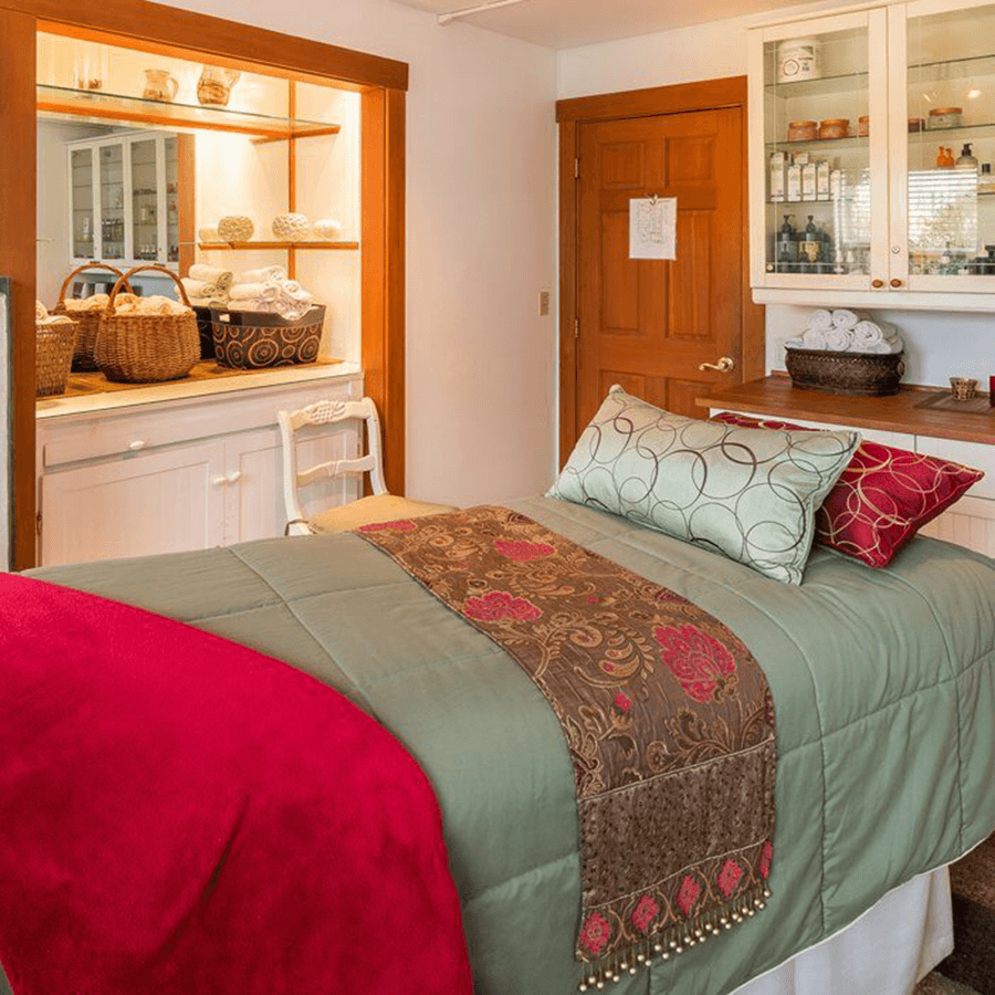 A cozy bedroom featuring a neatly made bed with decorative pillows and a colorful throw, alongside shelves filled with baskets and towels.