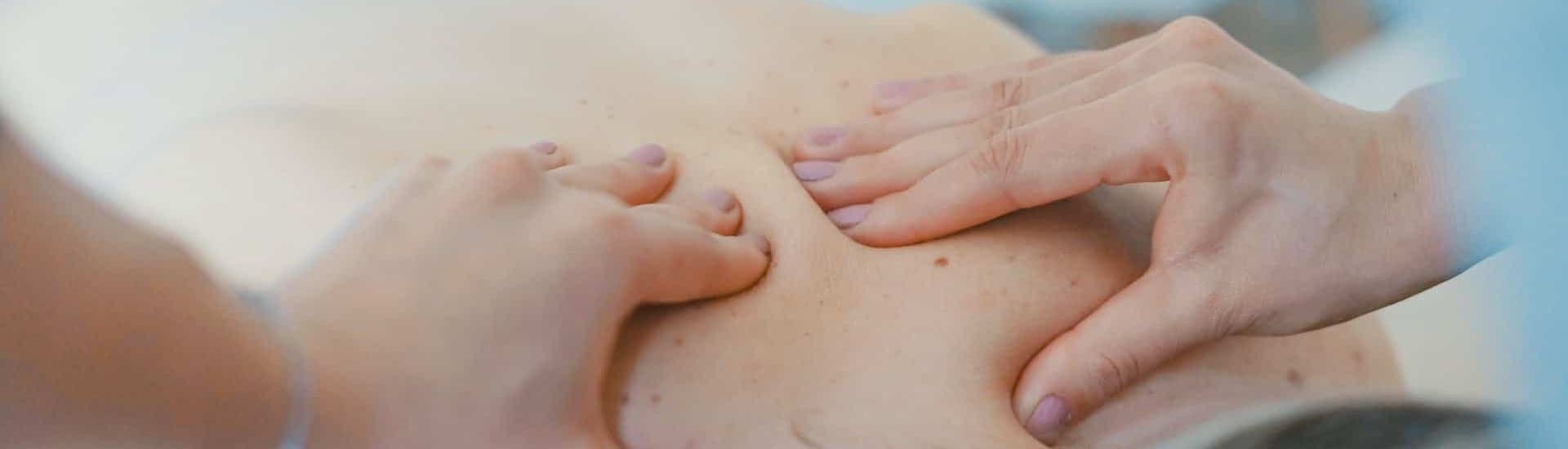A close-up of hands applying massage pressure on a person's back.
